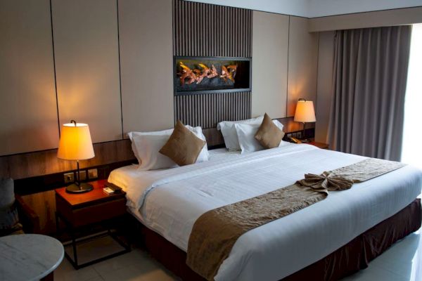 A hotel room with a large bed, two lamps, decorative cushions, and folded towels on the bed, with curtains on the side.