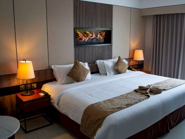 A hotel room with a large bed, two lamps, decorative cushions, and folded towels on the bed, with curtains on the side.