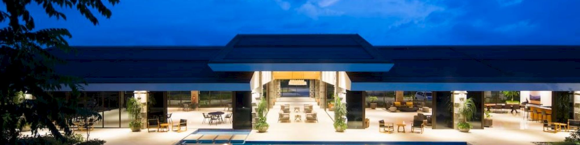 The image shows a luxurious building with large pools in front, lit at night, surrounded by a serene ambiance.