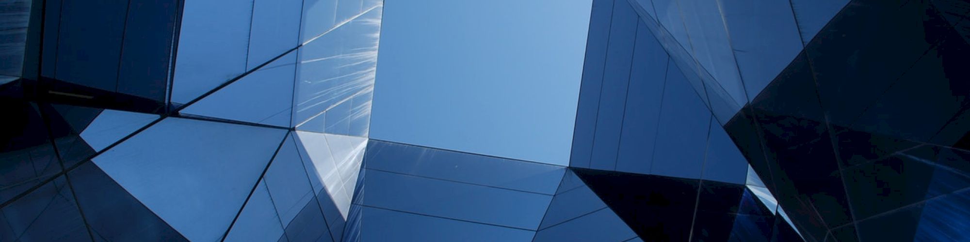 Sky as seen through a geometric pattern of reflective glass surfaces, creating an abstract architectural view.
