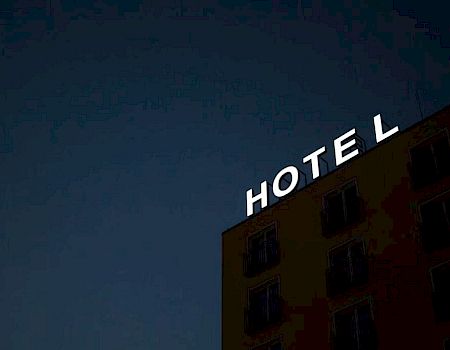 A dark building with illuminated letters spelling "HOTEL," missing the letter "L" at the top against a night sky.