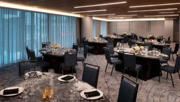 The image shows an elegantly set dining hall with round tables, black chairs, and soft lighting, ready for an event or banquet.