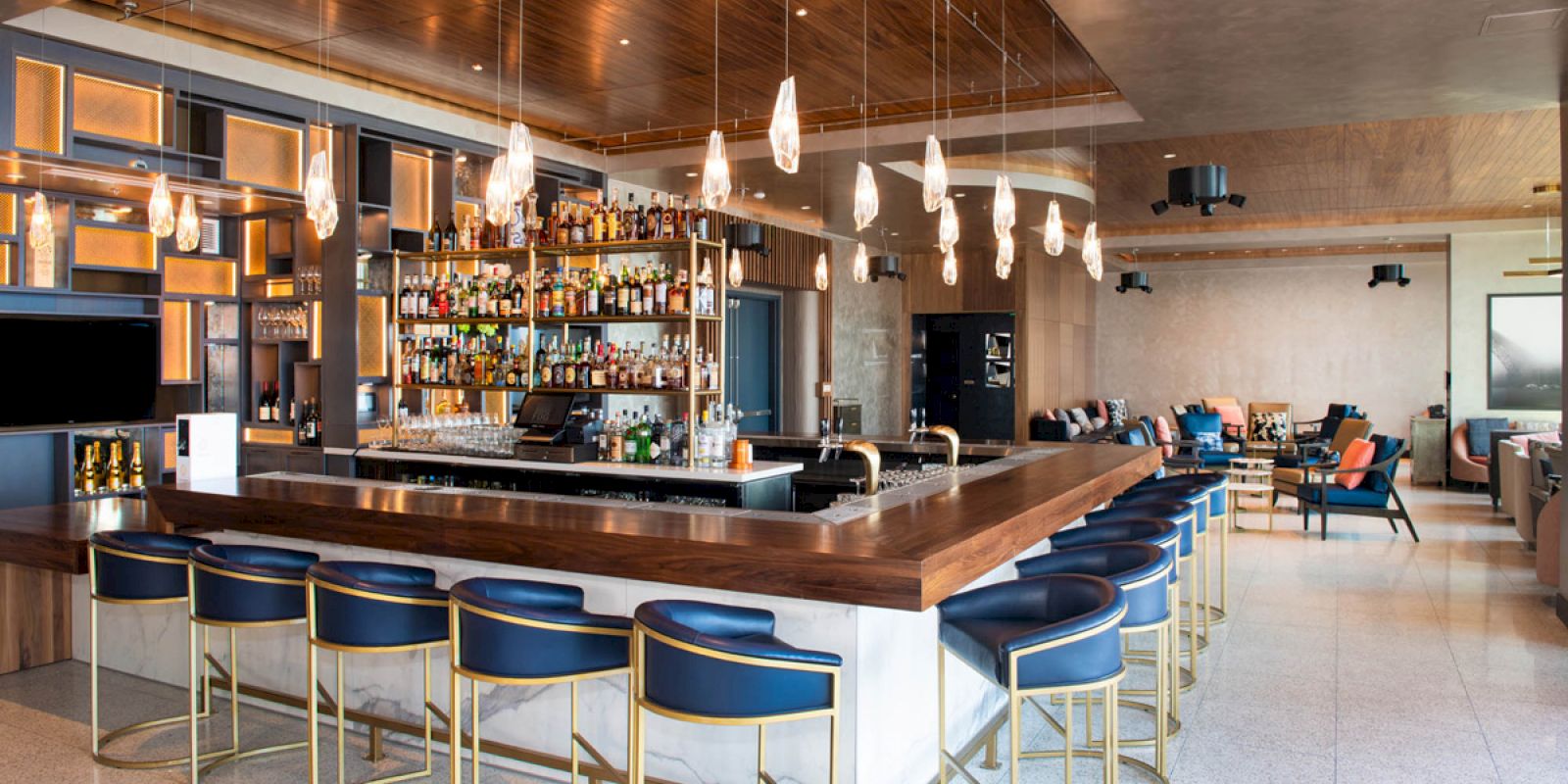 A modern bar with a large selection of bottles, stylish pendant lights, and bar stools in an upscale lounge setting.