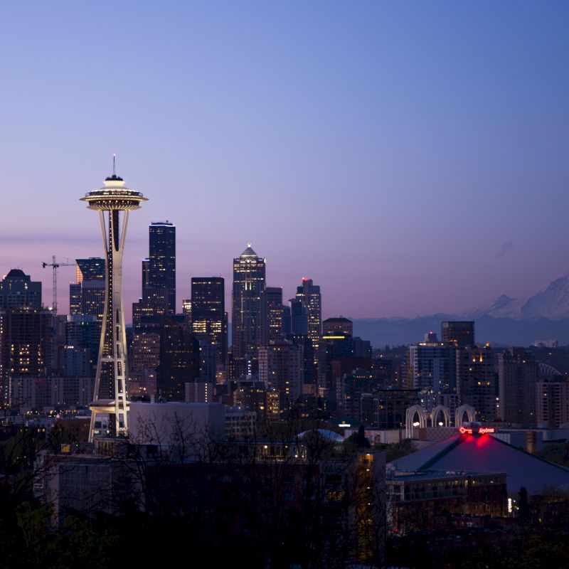 Seattle skyline at dusk with the Space Needle, city lights, and Mount Rainier in the background.
