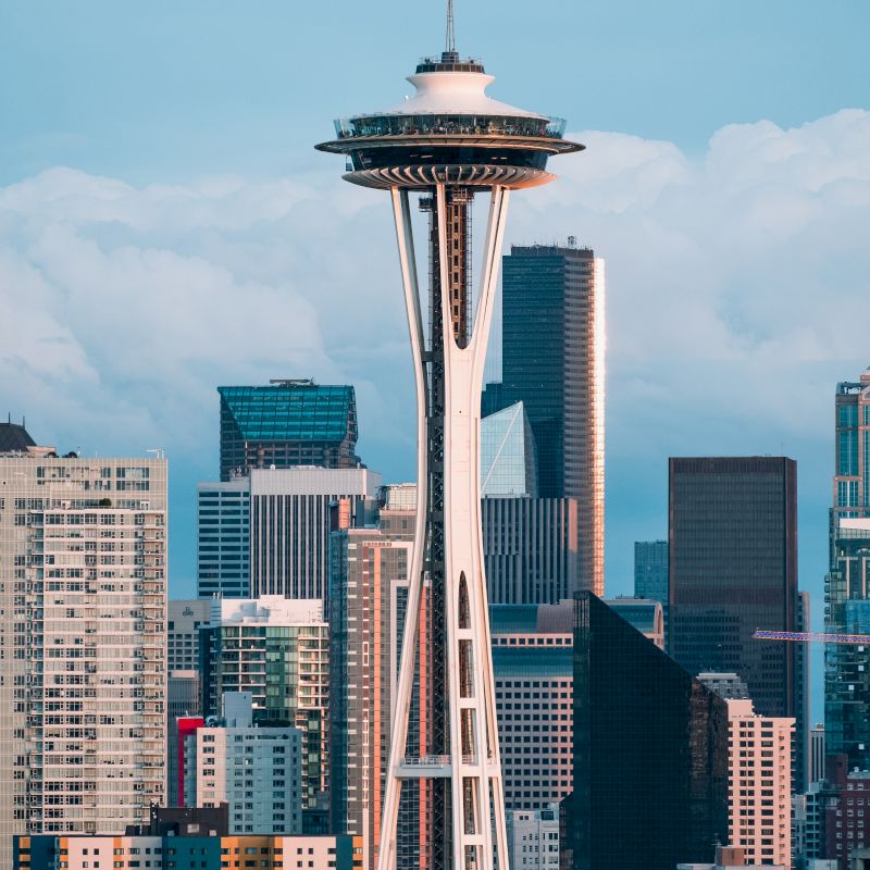 The image shows the Space Needle with Seattle's skyline in the background. Buildings and a cloudy sky complete the scene.