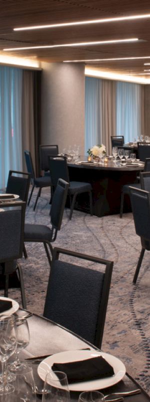 The image shows a dining setup in an elegant ballroom with round tables, chairs, tableware, and dim lighting, ready for an event.
