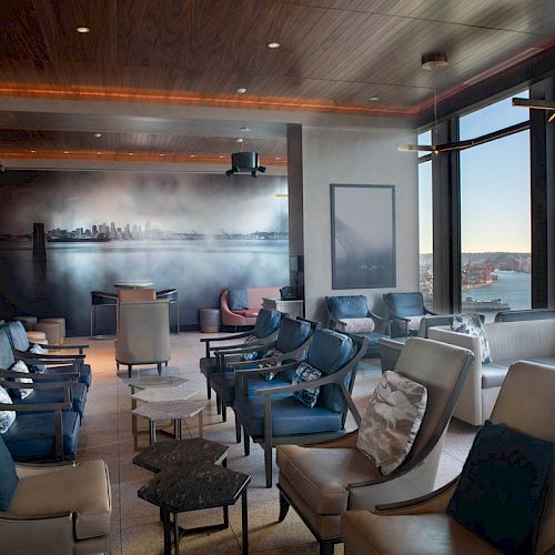 A modern lounge with comfortable seating, a cityscape mural, and large windows offering a scenic view, including a Ferris wheel in the distance.