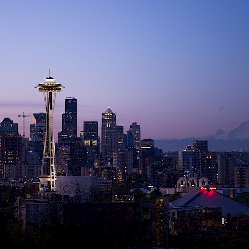 Seattle skyline at dusk featuring the Space Needle, city buildings, and Mount Rainier in the background under a purple sky.