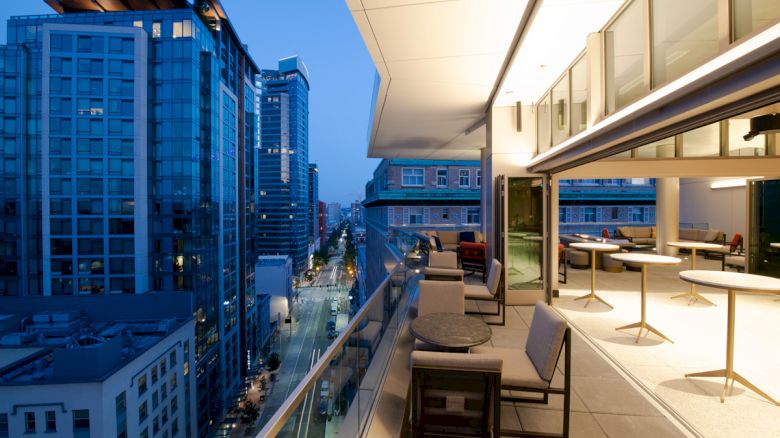 A modern cityscape at dusk with high-rise buildings and an elegant outdoor terrace featuring tables and chairs.