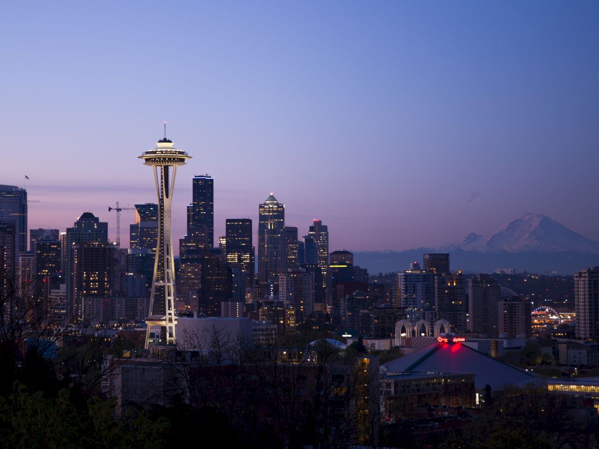 The image shows a nighttime view of Seattle's skyline with the Space Needle and Mount Rainier visible in the background.