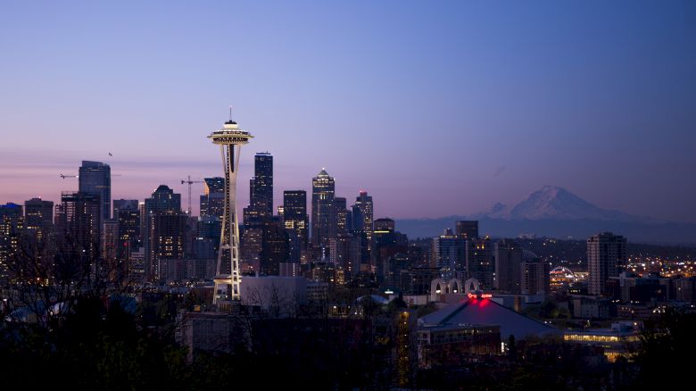 The image shows a nighttime view of Seattle's skyline with the Space Needle and Mount Rainier visible in the background.